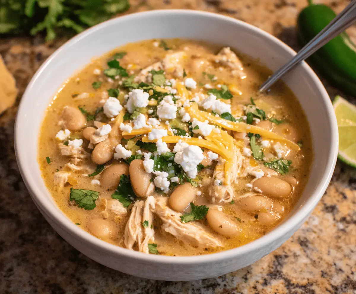 Creamy white chicken chili topped with shredded cheese and fresh cilantro in a bowl, served with tortilla chips on the side.
