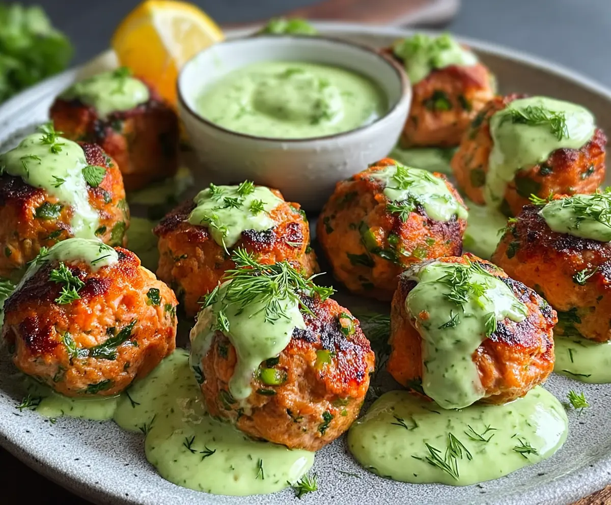 Delicious baked salmon meatballs served with a creamy tangy avocado sauce on a white plate.
