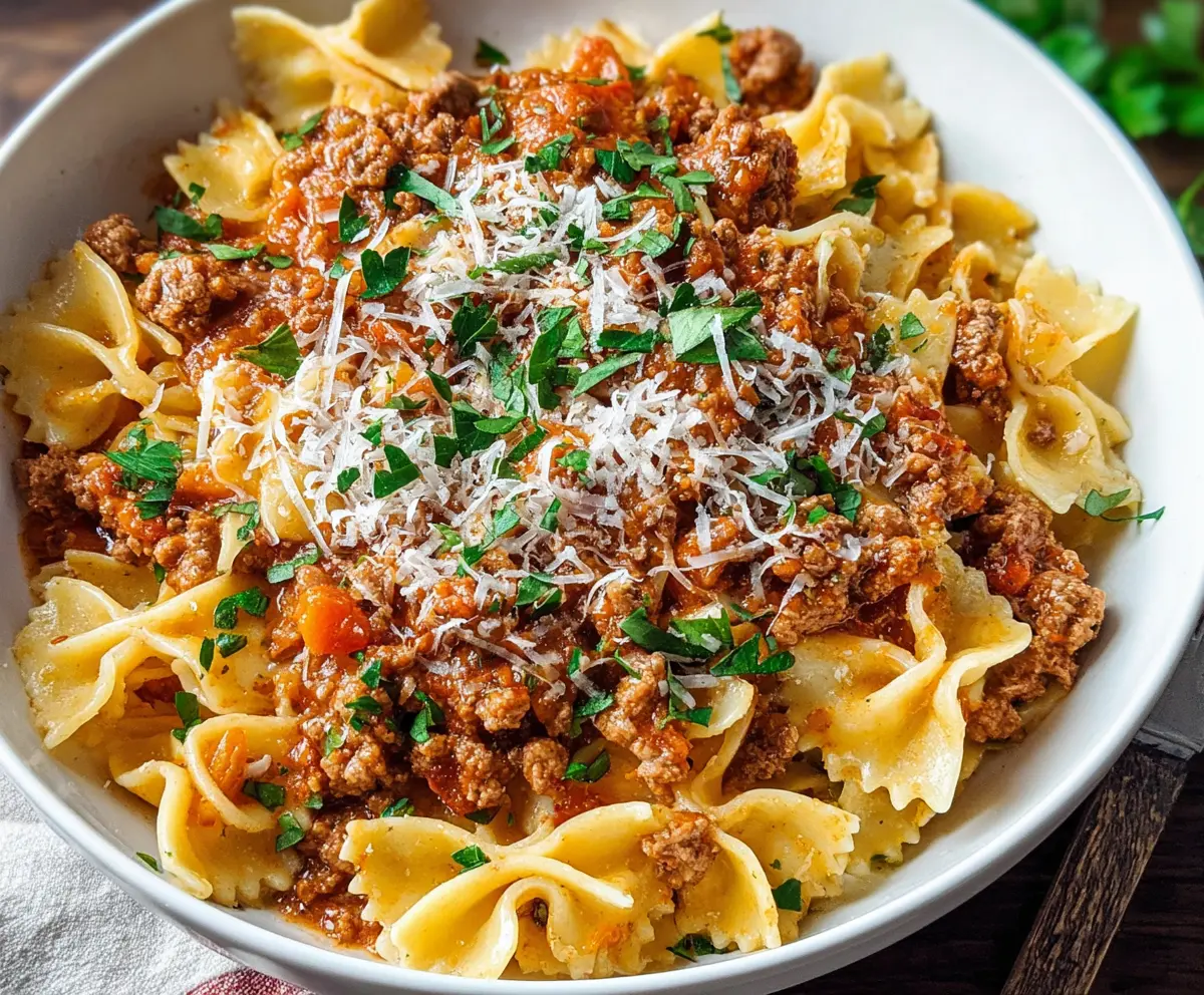 Delicious pork Bolognese pasta served in a white bowl, garnished with herbs.