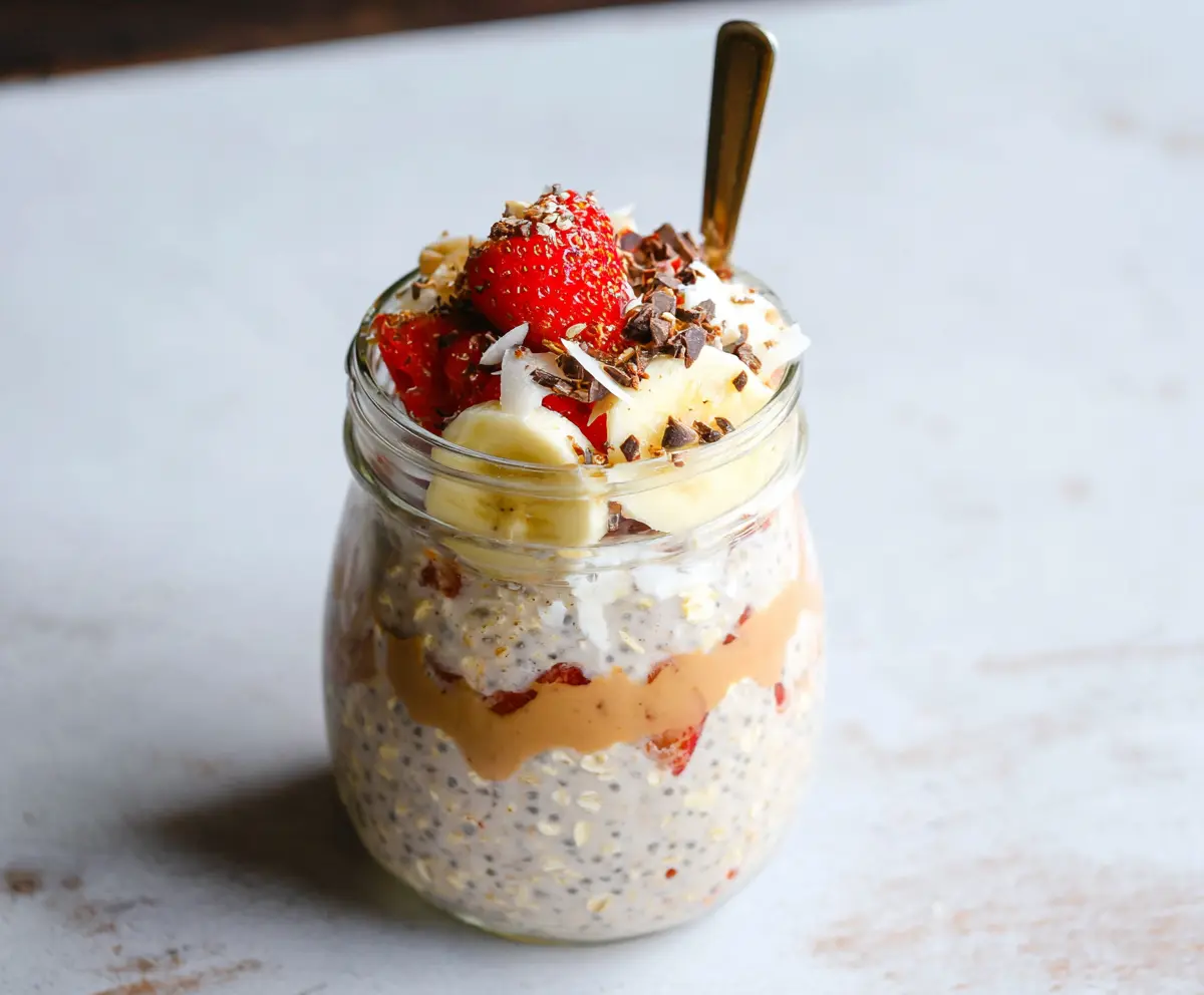 Banana Split Overnight Oats topped with sliced bananas, strawberries, chocolate syrup, and whipped cream in a jar