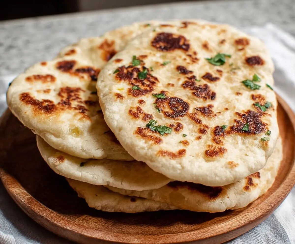 Homemade sourdough discard naan bread on a wooden serving board, showcasing its soft and fluffy texture.