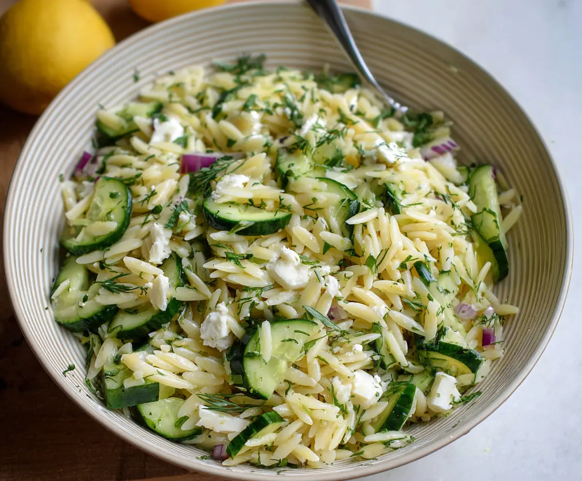 Refreshing Cucumber Lemon Orzo Salad in a glass bowl with fresh herbs and lemon slices.