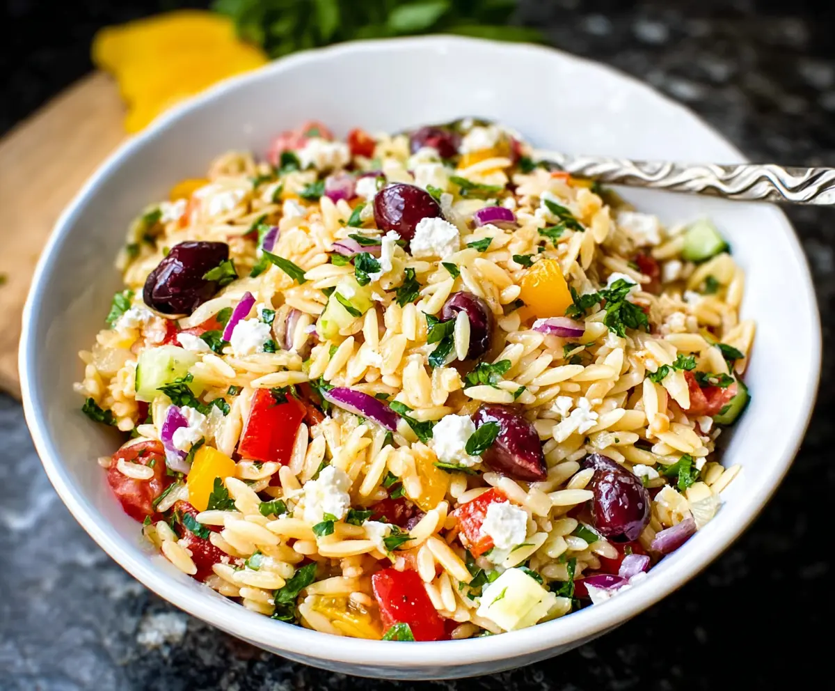 Fresh Greek Orzo Salad with cucumbers, tomatoes, feta cheese, and herbs on a decorative plate.