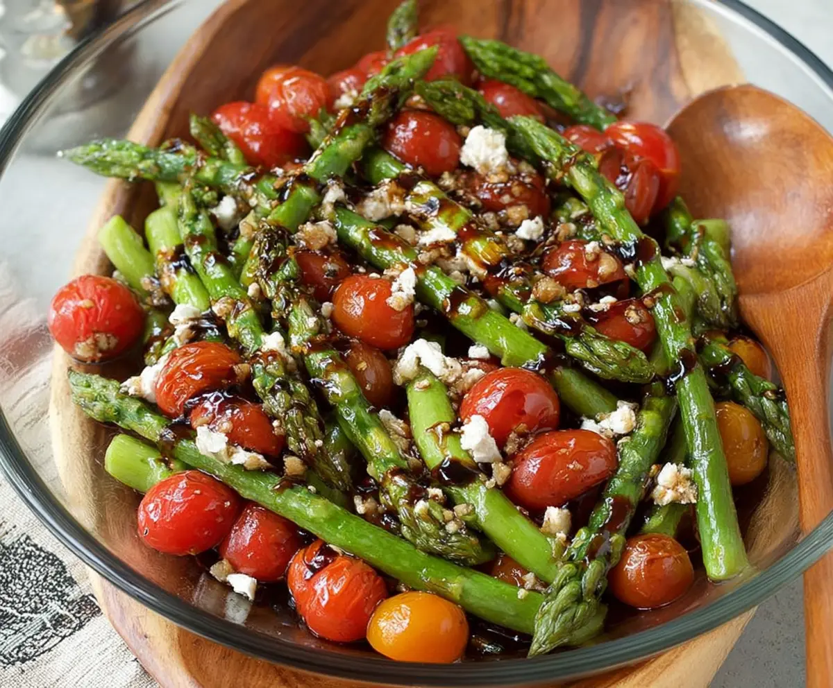 Fresh balsamic asparagus and tomato salad garnished with herbs on a white plate.