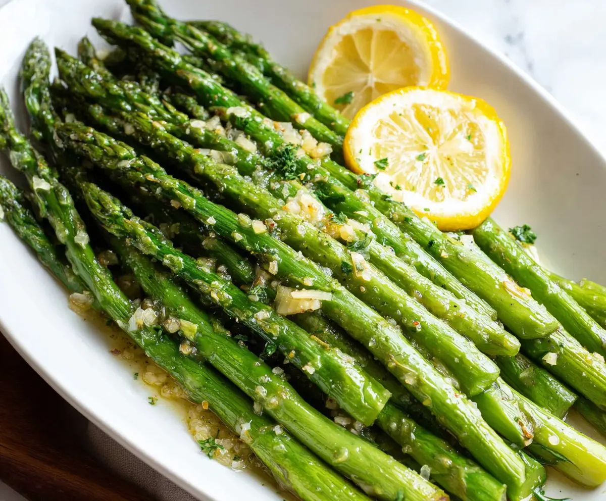 Delicious Lemon Garlic Asparagus on a white plate with fresh lemon slices